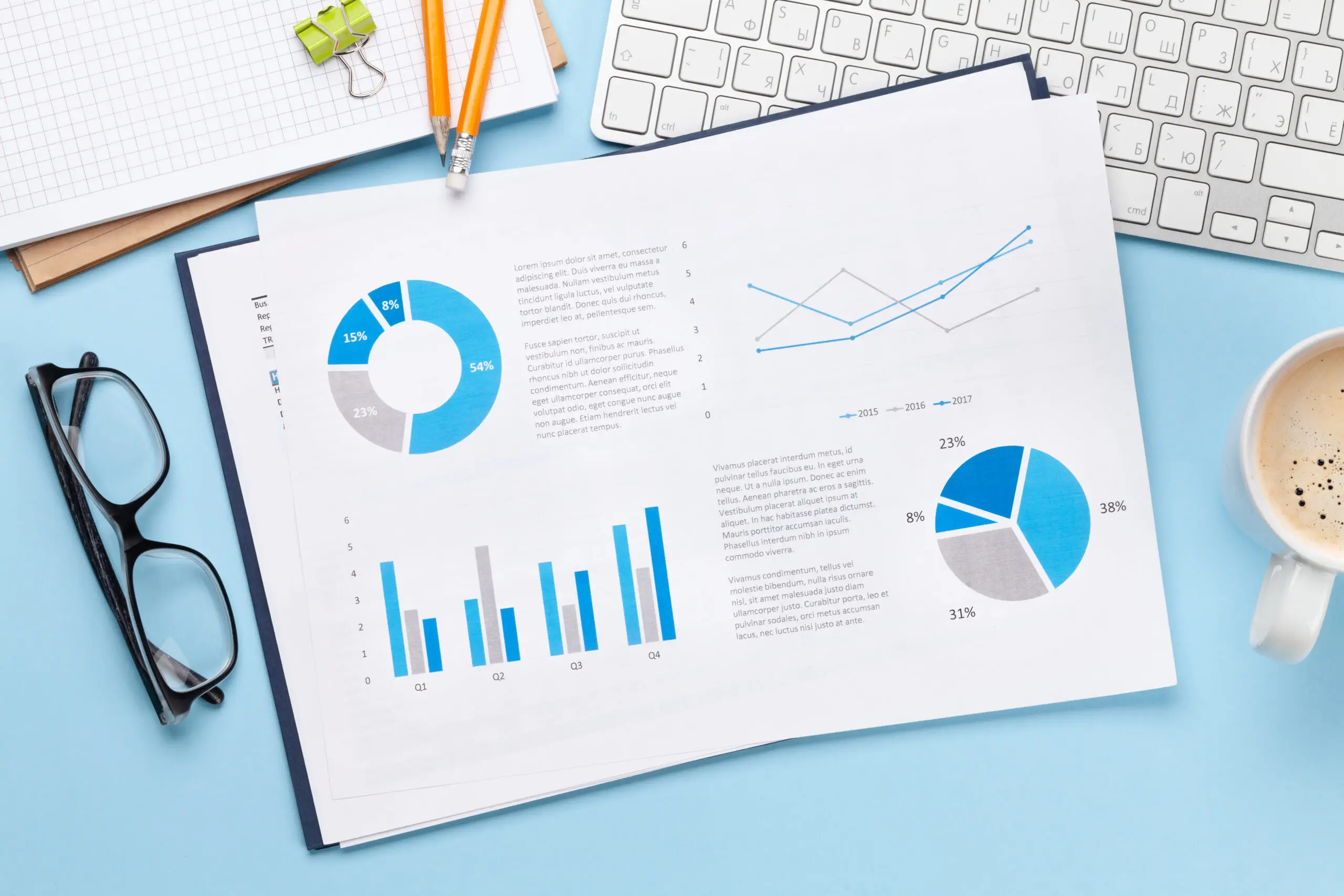 A step-by-step guide to long-term digital success. A desk with a keyboard, eyeglasses, a cup of coffee, and a sheet featuring blue and gray charts and graphs for a step-by-step guide to long-term digital success.